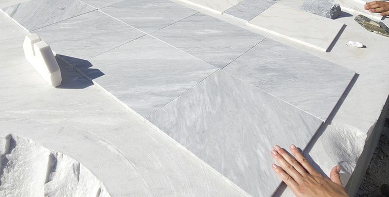 Hand raakt een diagonaal patroon van marmeren tegels aan. De tegels zijn wit met grijze aders.