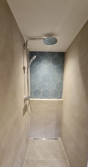 Douchecabine met blauwe zeshoekige tegelaccenten en chromen armaturen. Beige muren en vloer.