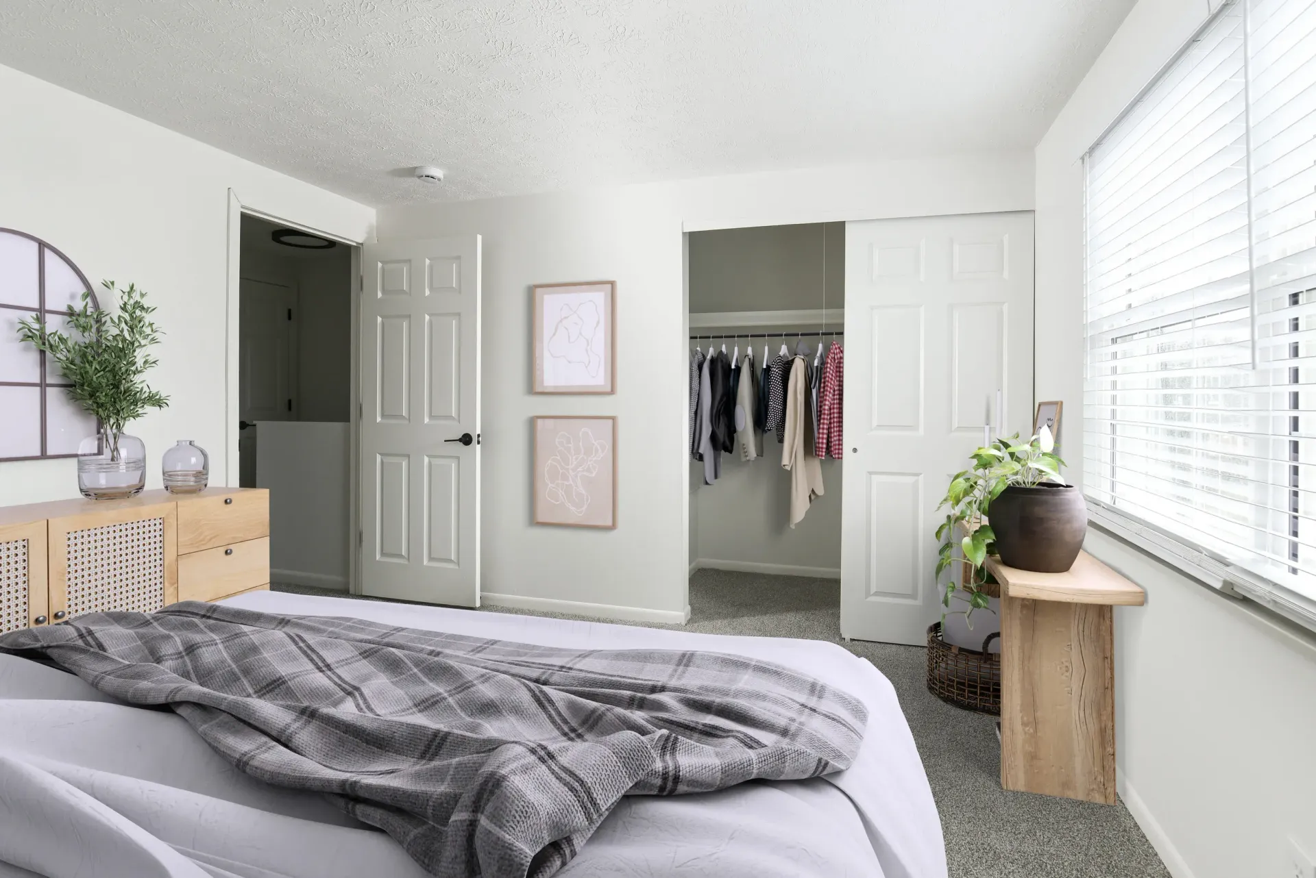 Bedroom with bed in foreground, open closet with clothes, a window with blinds, and a dresser.