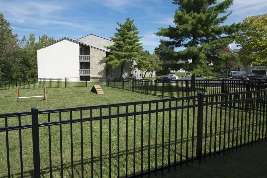 Exterior view of a multifamily complex with a fenced grassy yard and buildings in the background.