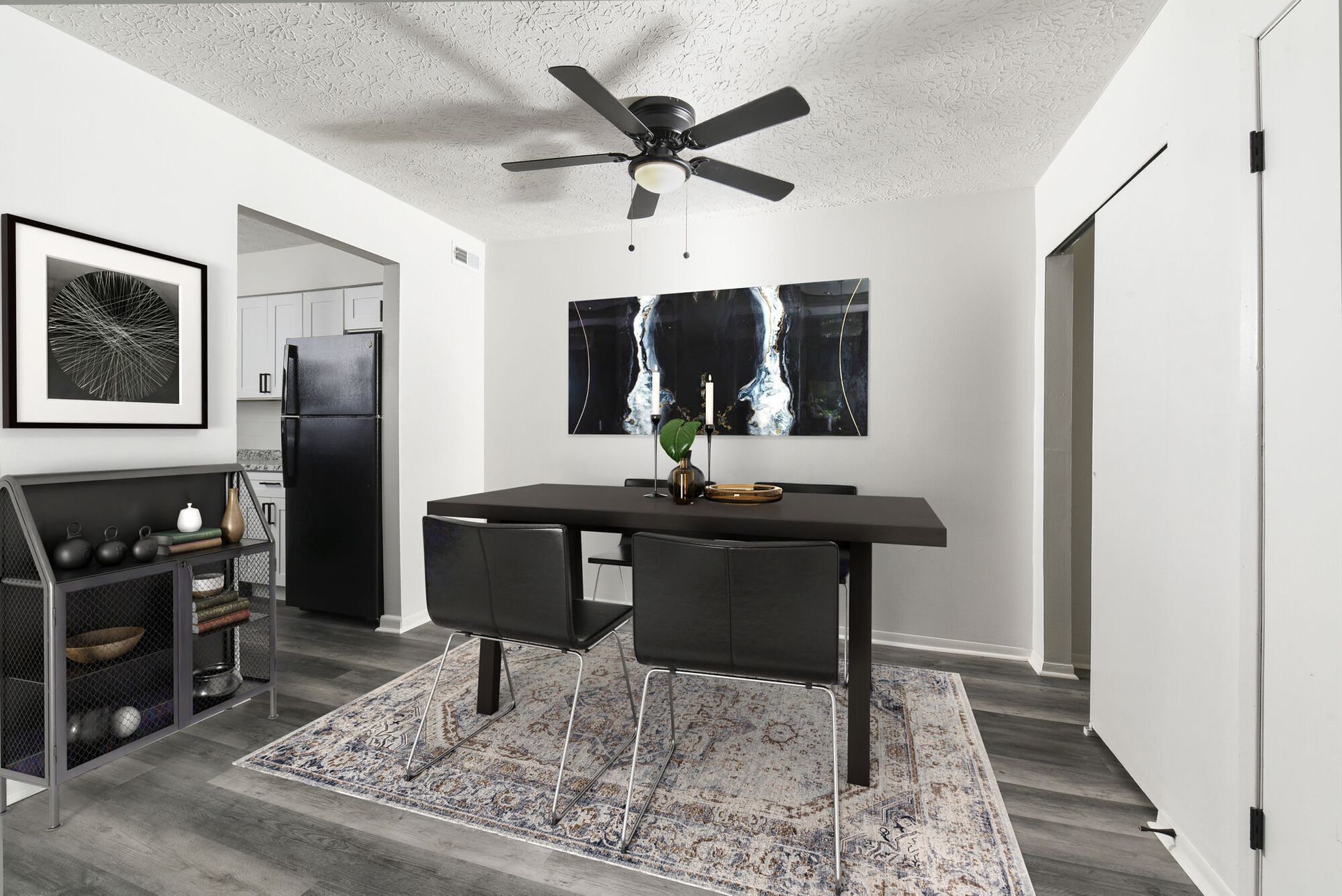 Dining area in a modern apartment with a dark table, black chairs, ceiling fan, and abstract wall art.