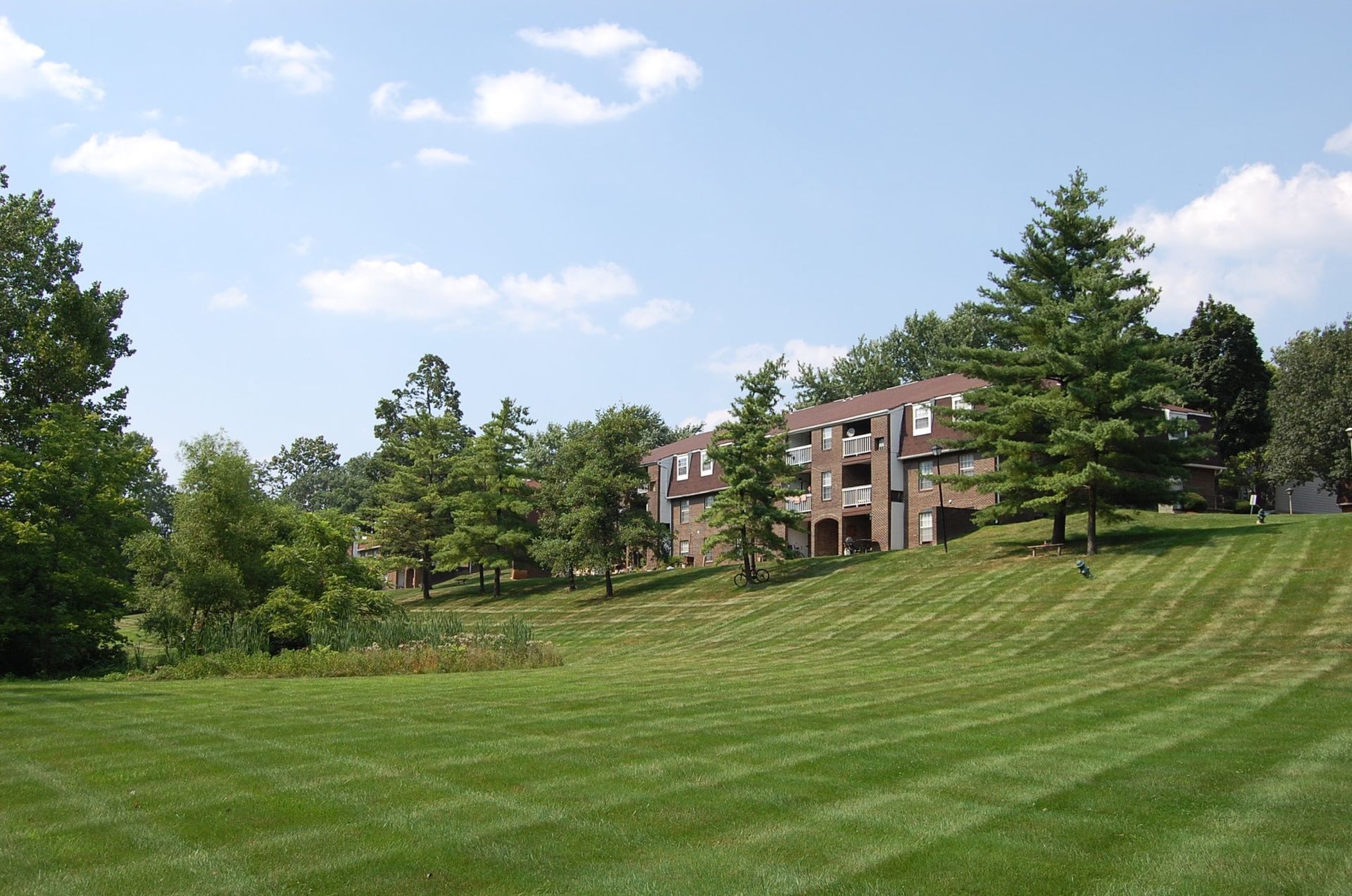 Exterior view of a brick apartment community with a well-kept lawn and trees.