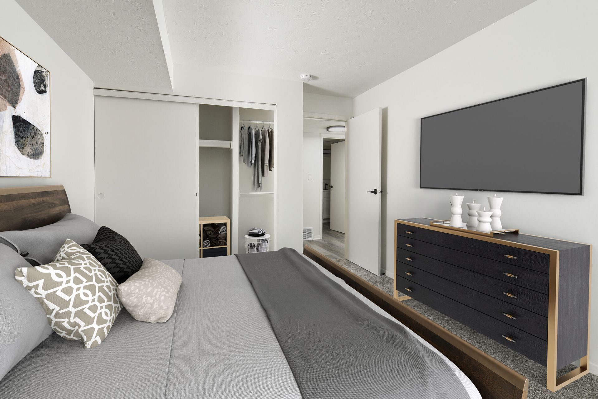 Bedroom in a modern apartment with a bed, dresser, wall-mounted TV, and open closet.