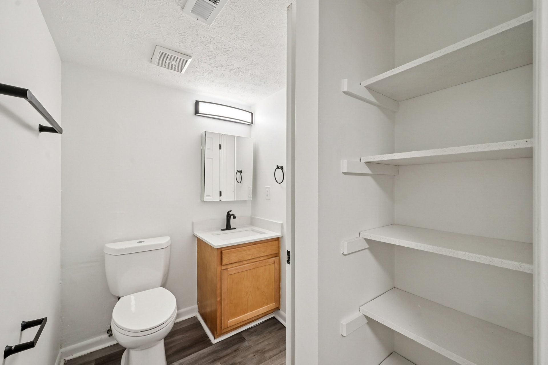 Apartment bathroom with toilet, vanity sink, mirror, and open linen closet.