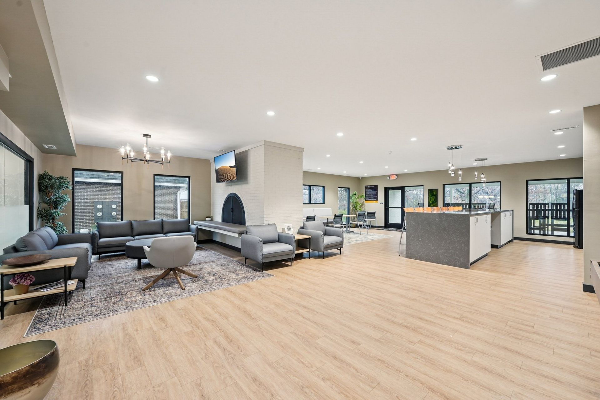 Interior of a modern apartment community lounge with sofas, chairs, a fireplace, and a kitchen island.