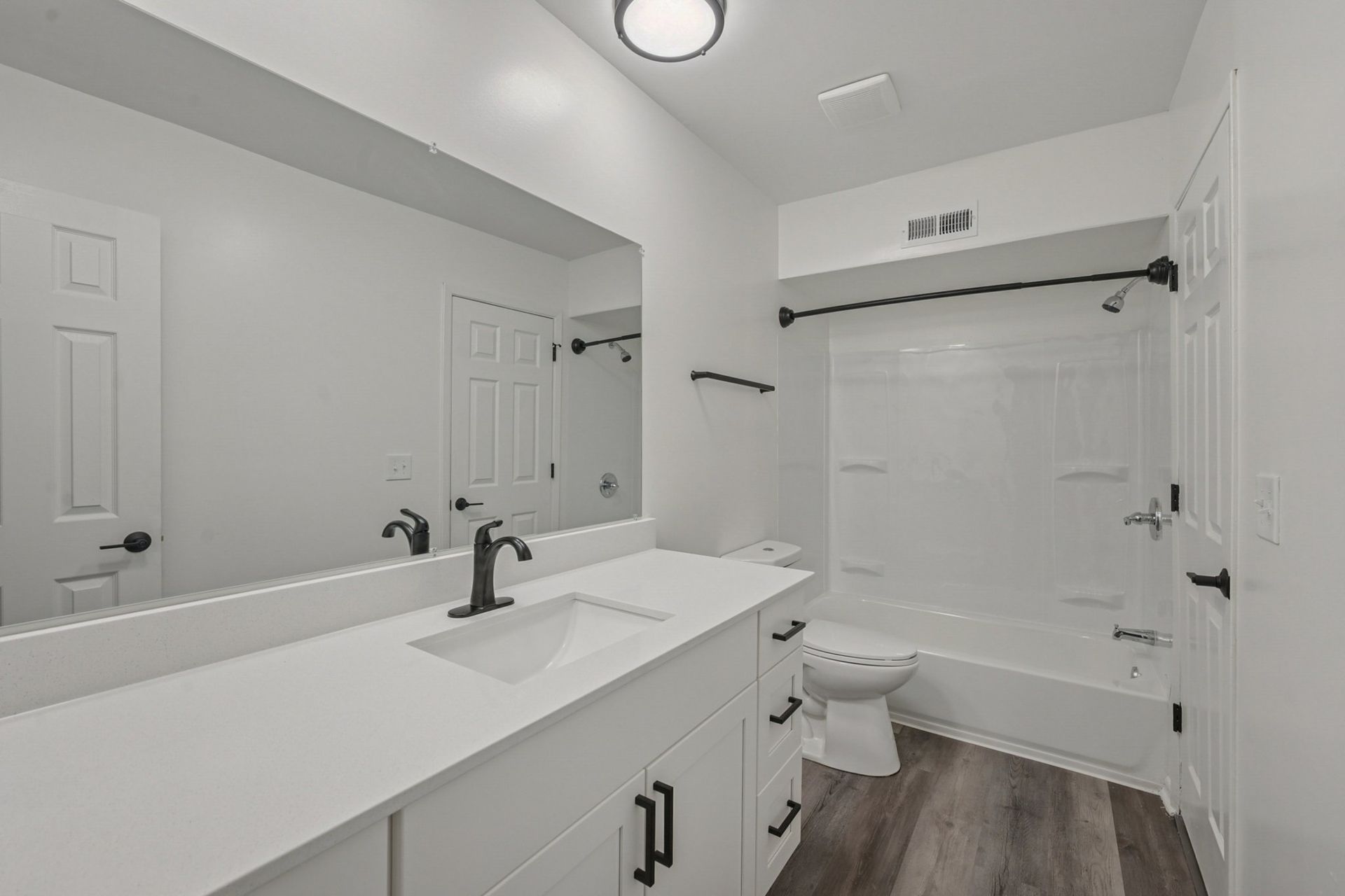 White bathroom with a large vanity, mirror, toilet, and a bathtub/shower.