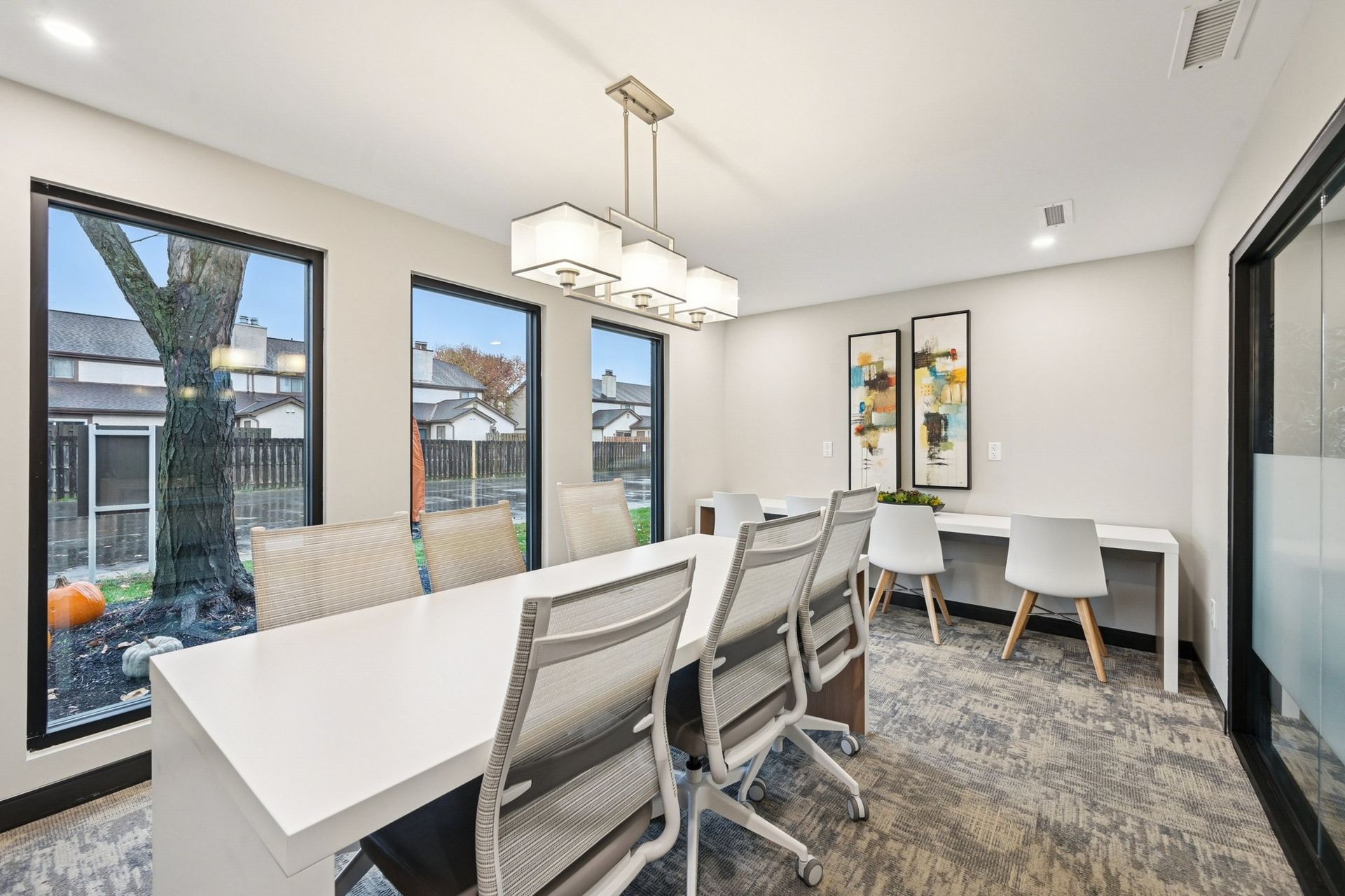 Bright, contemporary community meeting room with a long white table and white chairs by large windows.