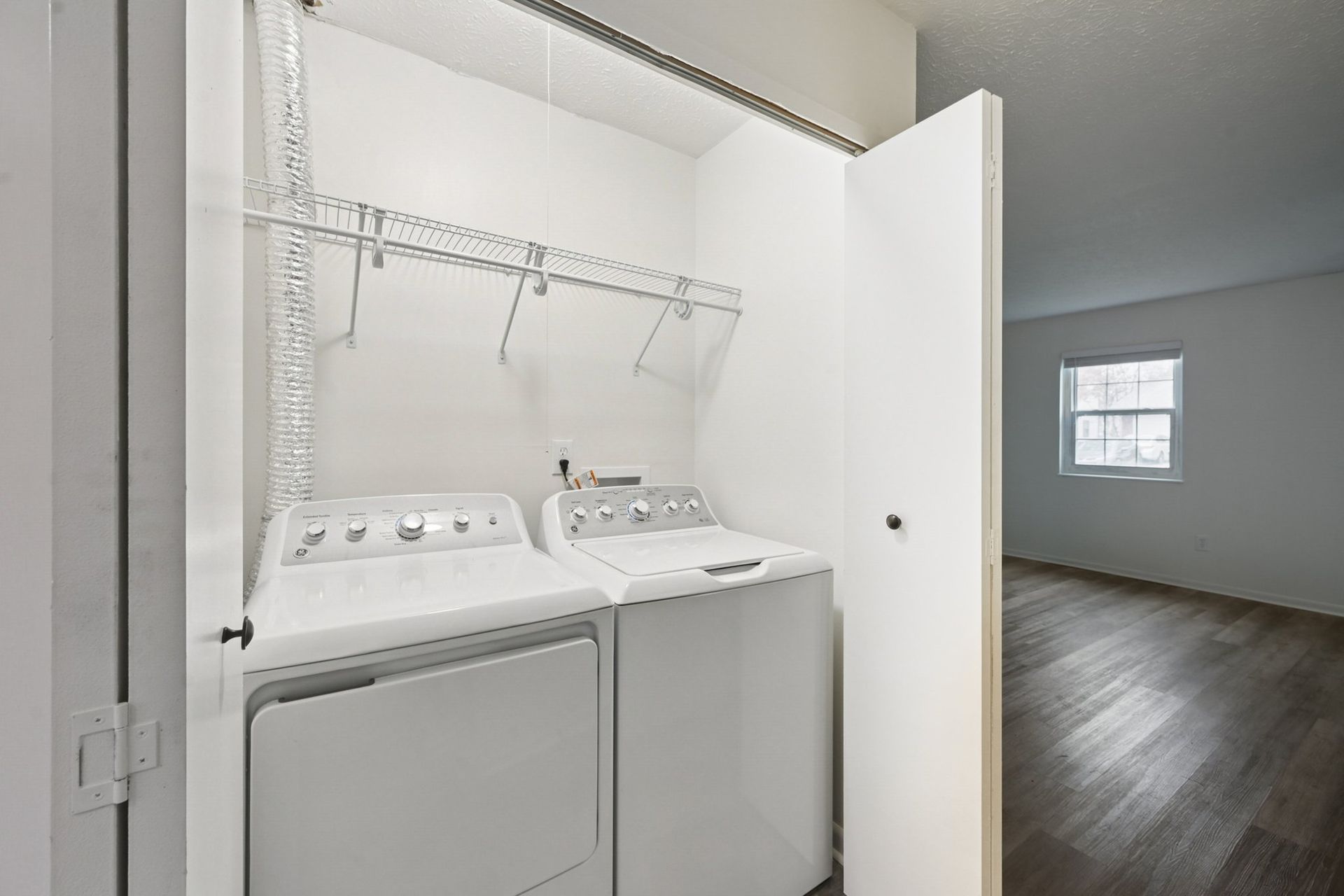 In-unit laundry closet with white washer and dryer and a wire shelf.