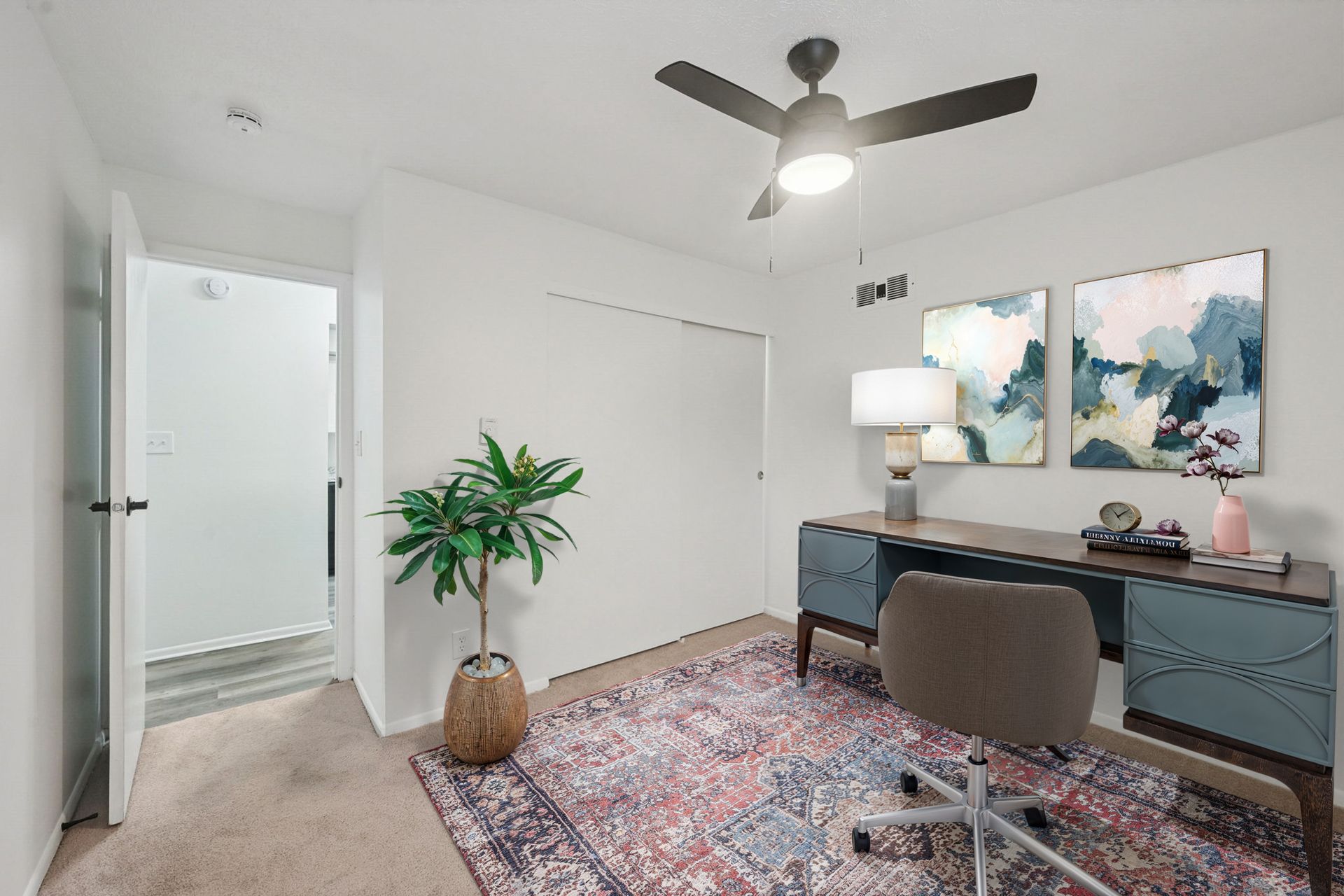 Interior home office in an apartment with desk, chair, plant, rug, and wall art.