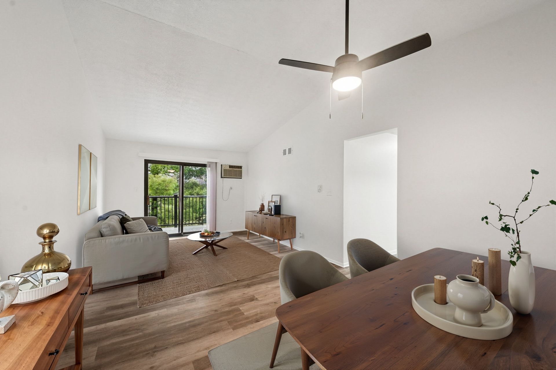 Bright living room with white walls, wood floors, beige sofa, dining table, and sliding balcony door.