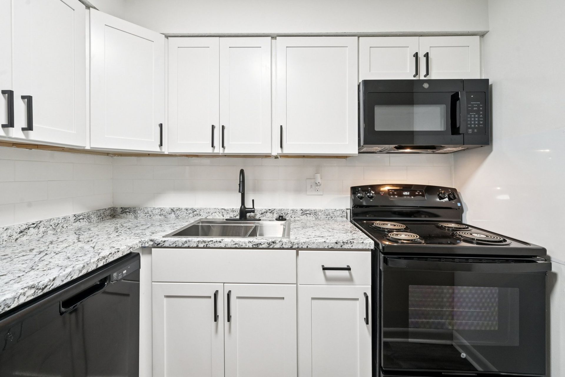 Modern apartment kitchen with white cabinets, granite countertops, sink, and black appliances.