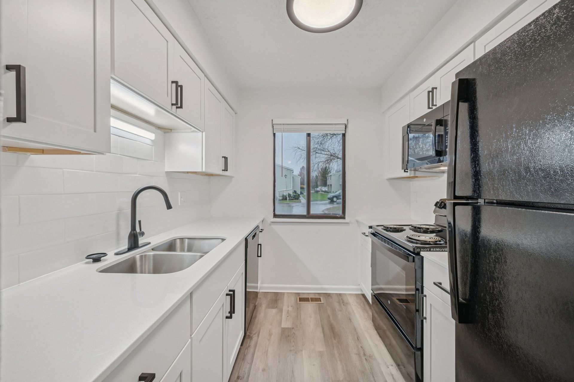 Galley-style white kitchen with double sink, black faucet, and stainless appliances.