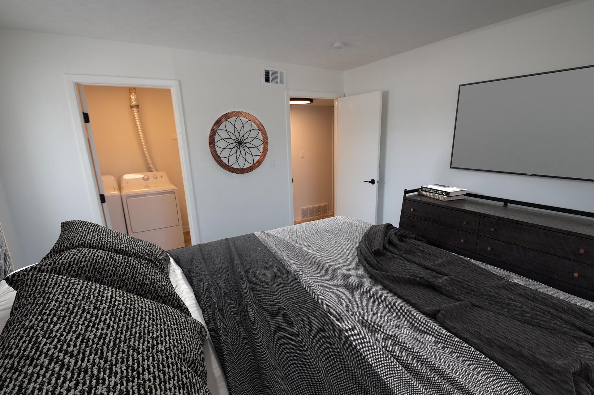Bedroom with a large bed, dark dresser, mounted TV, and an open laundry closet to the left.