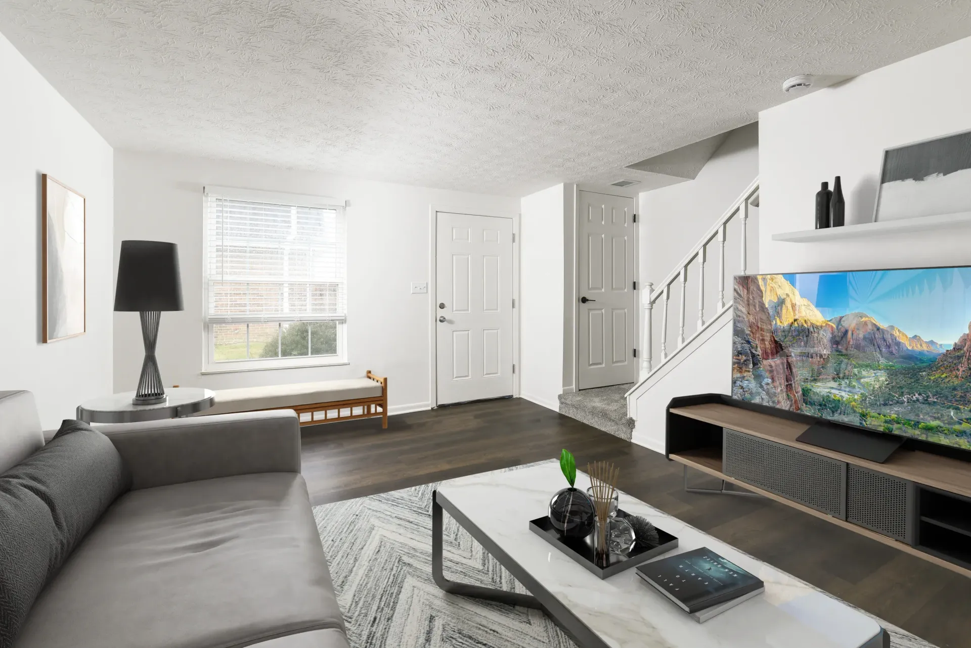 Living room in an apartment with a gray sofa, marble coffee table, window, and staircase.