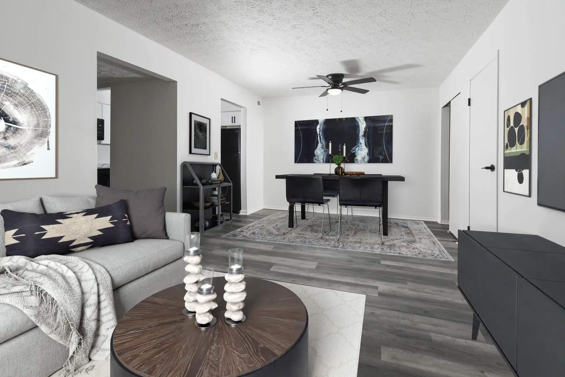 Open living/dining area with a gray sofa, round coffee table, dining table, and wall art.