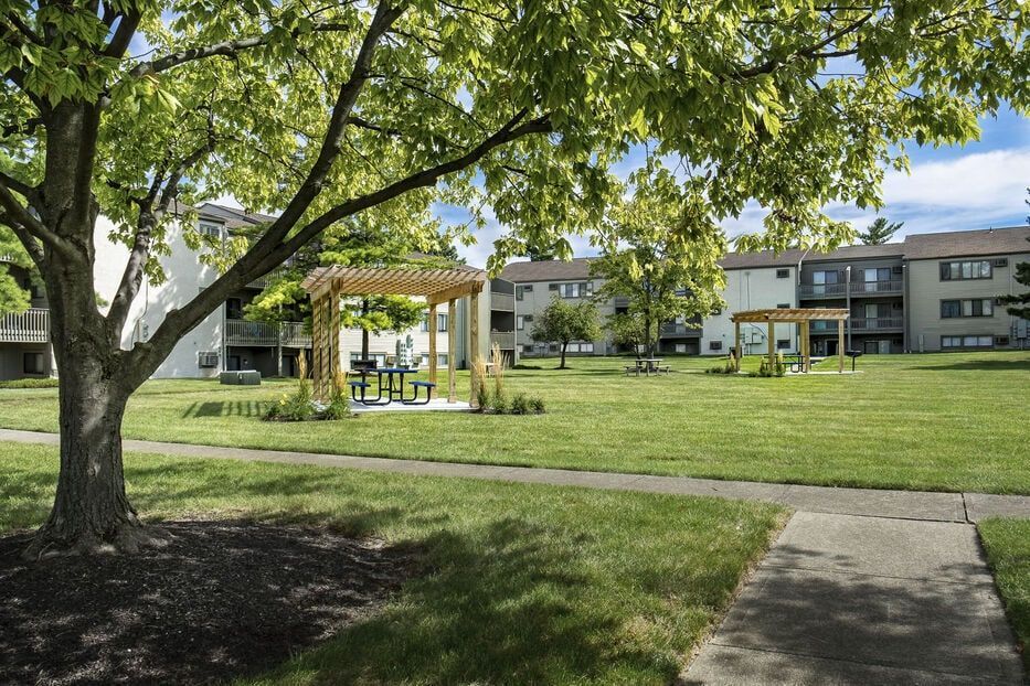 Shaded green lawn with trees, pergolas, and picnic tables in a multi-family property courtyard.