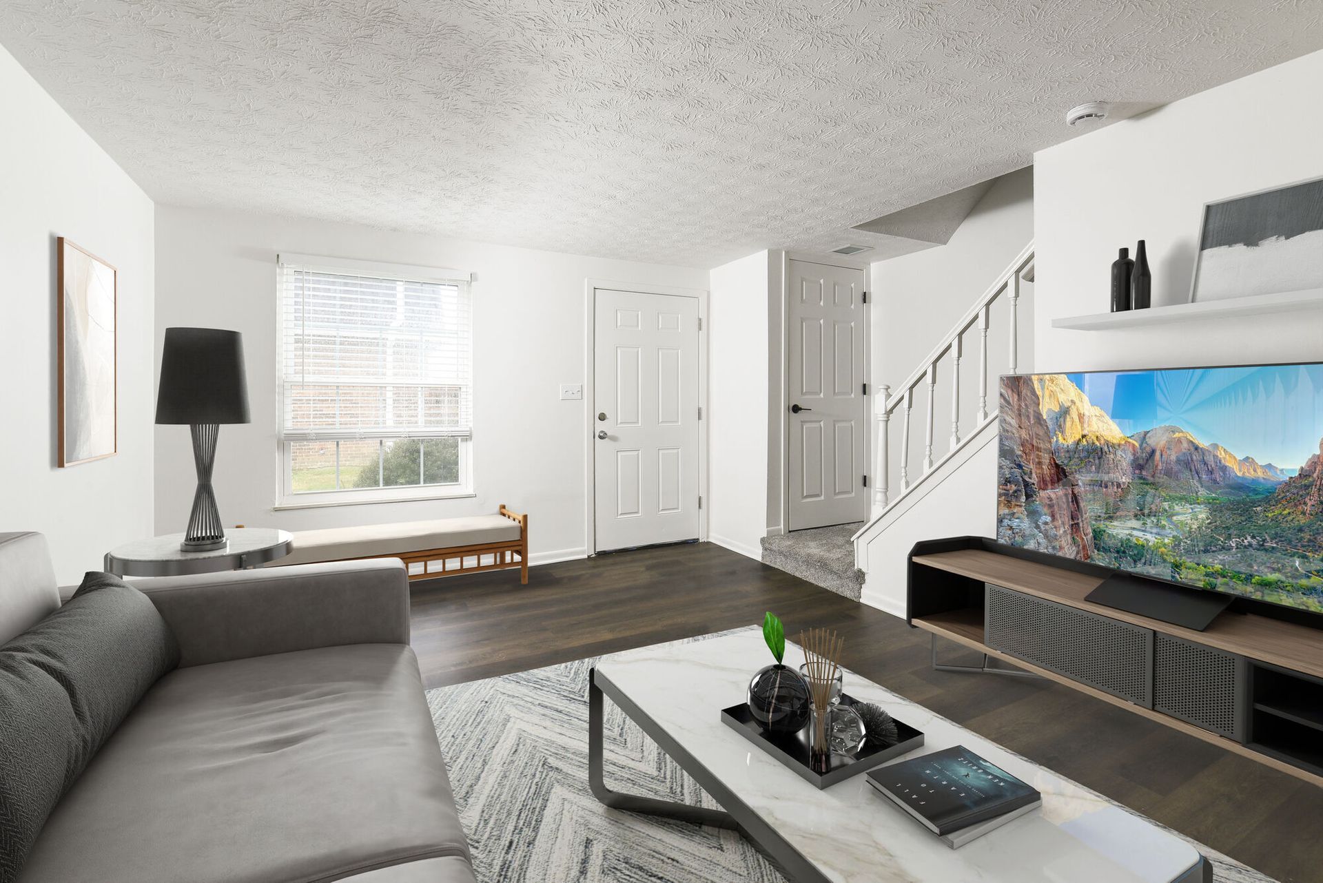 Living room of a modern apartment with a gray sofa, coffee table, and stairs.
