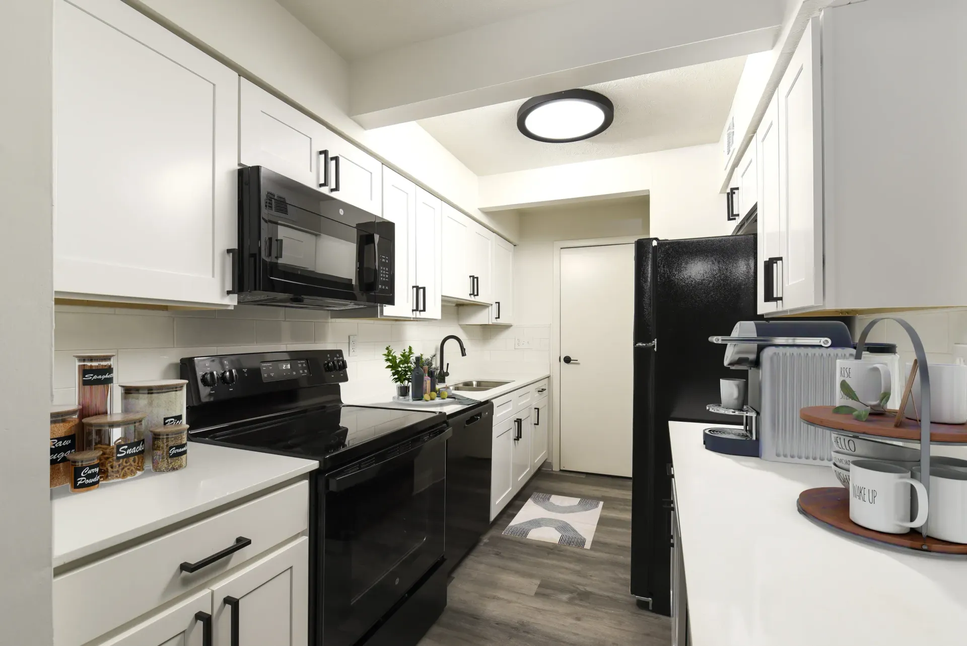 Modern apartment kitchen with white cabinets, black appliances, and a stainless sink.