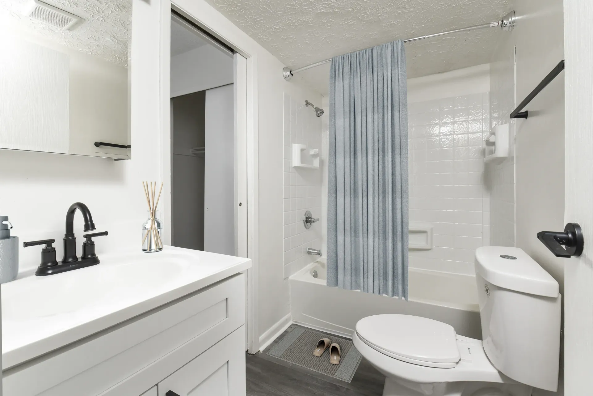 White bathroom with vanity, mirror, tub/shower, toilet, and a blue shower curtain.