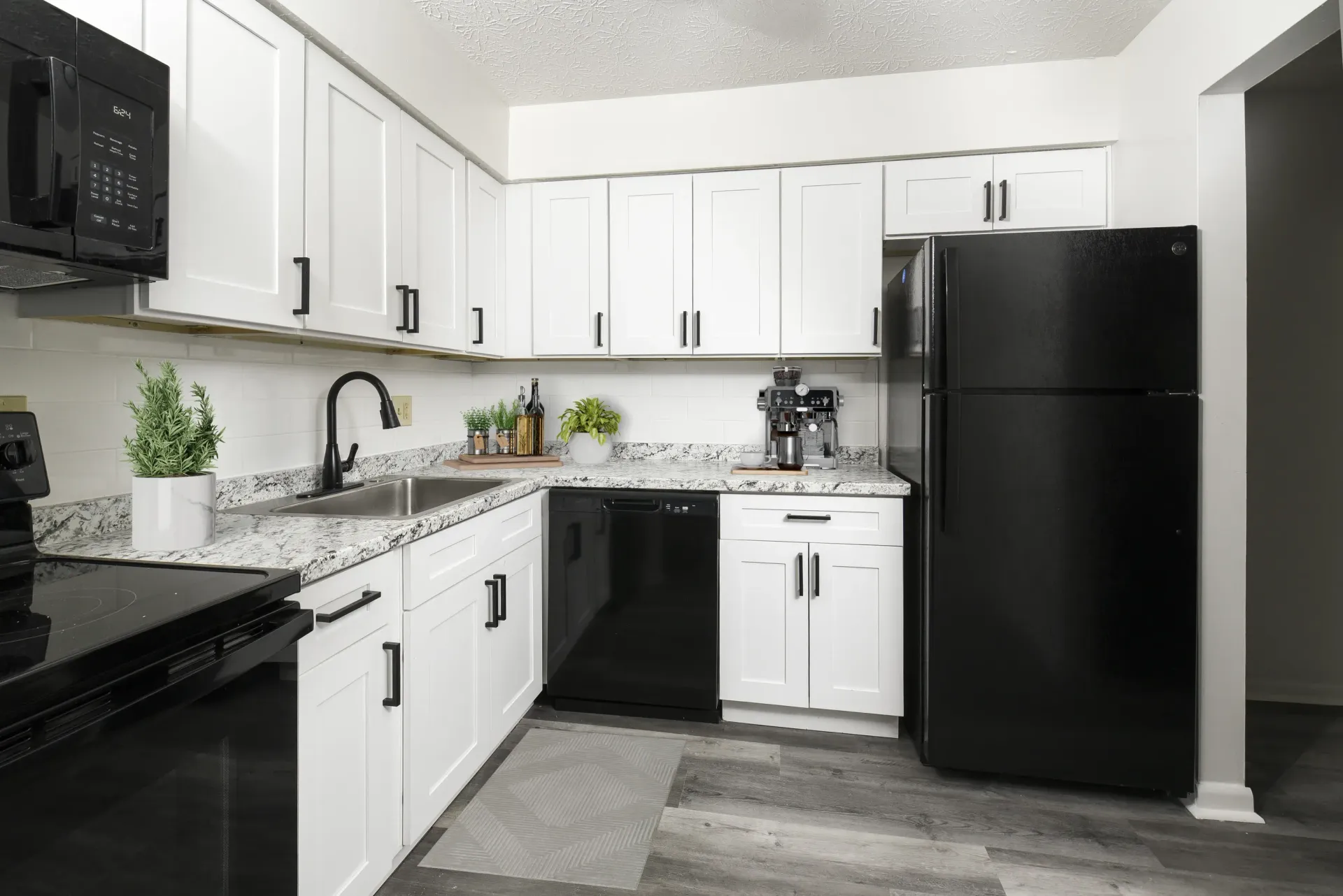 White kitchen with granite countertops, white cabinets, and black appliances.