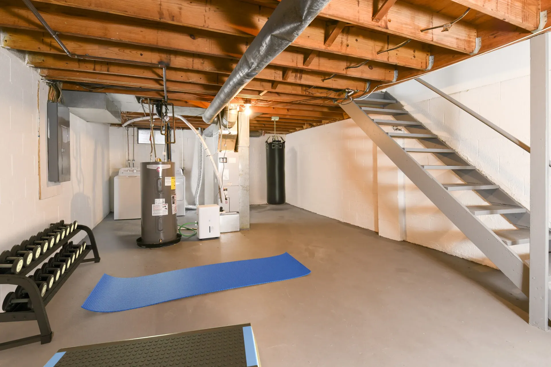 Basement fitness area with free weights, a punching bag, a blue mat, and stairs.