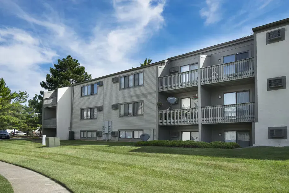 Exterior view of a gray, multi-story apartment building with balconies and a green lawn.