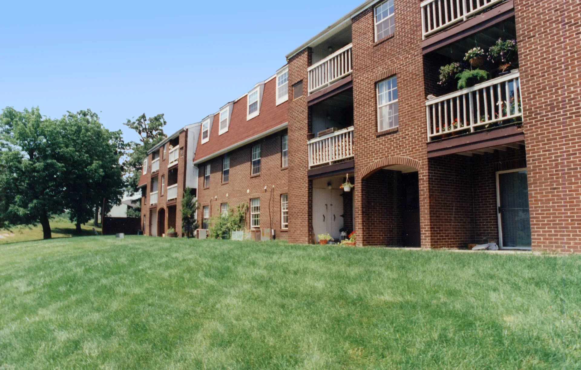 Exterior view of a brick apartment building with balconies and a grassy lawn.