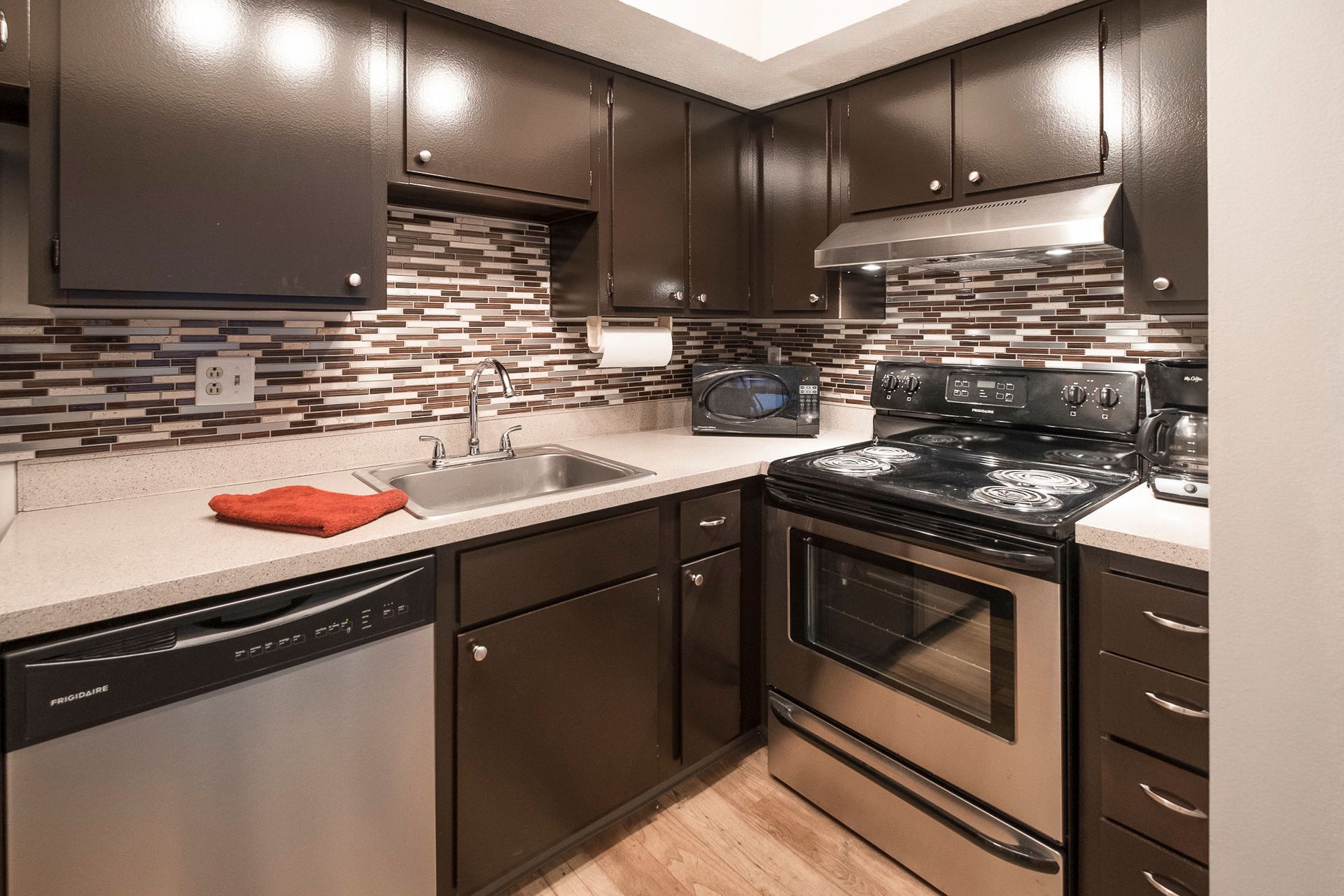Compact kitchen with dark cabinets, stainless appliances, and a mosaic tile backsplash.