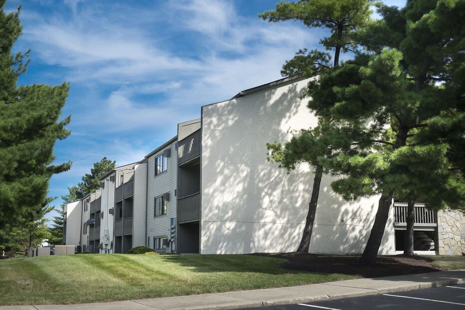 Exterior view of a multi-family apartment building surrounded by a grassy lawn and trees.