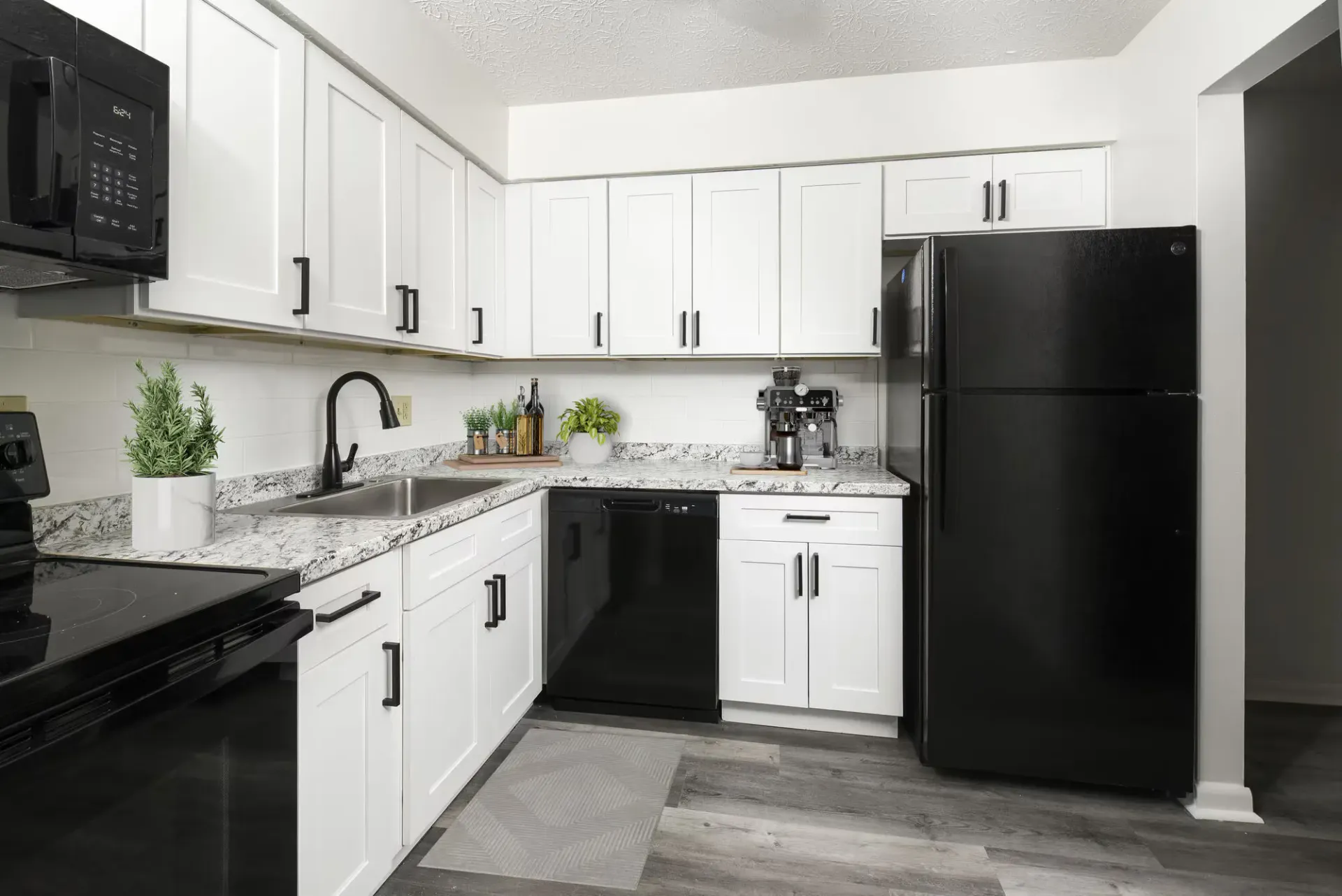 L-shaped kitchen in an apartment with white cabinets, granite counters, and black appliances.