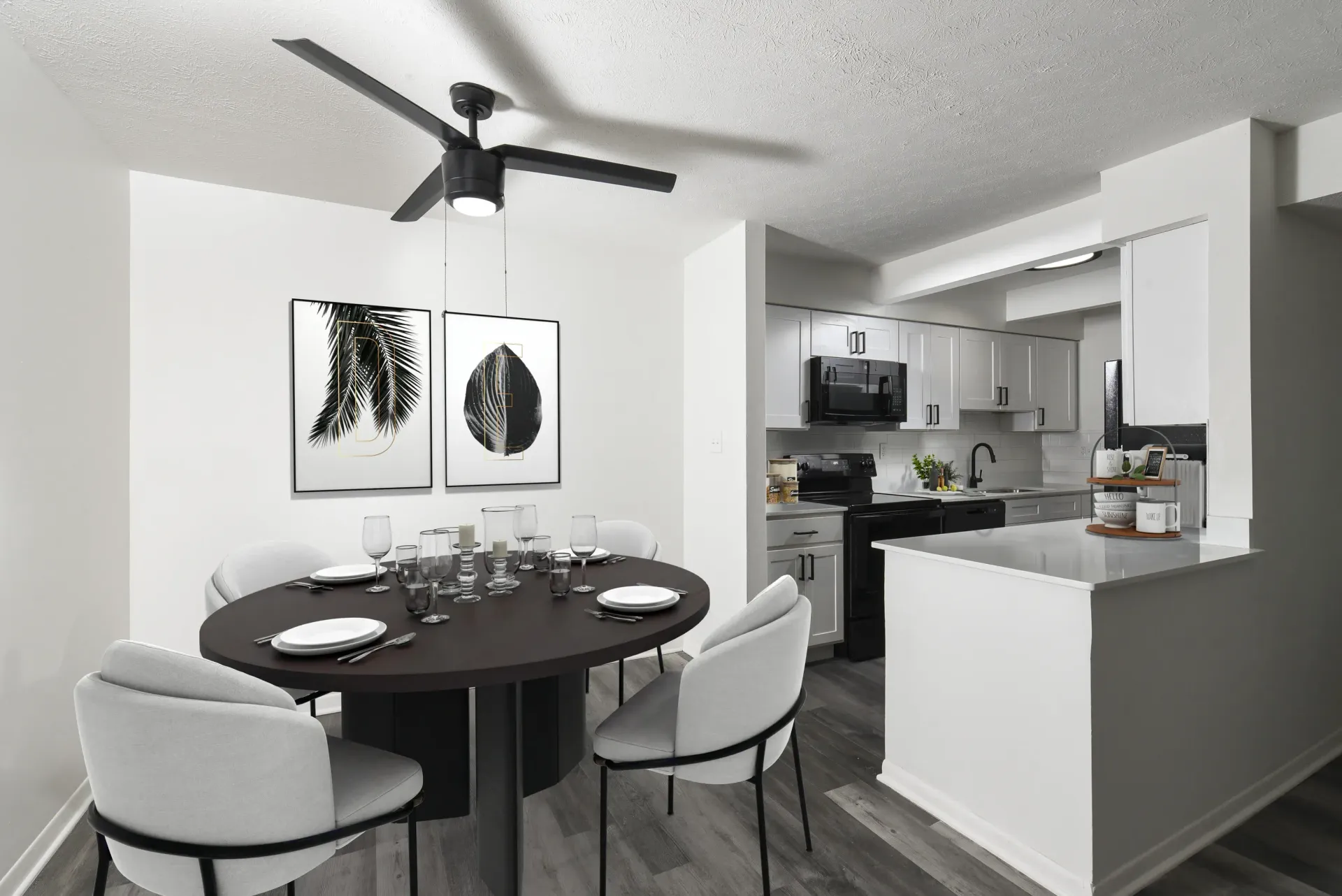 Round black dining table with four light gray chairs in a modern open-plan dining area and kitchen.