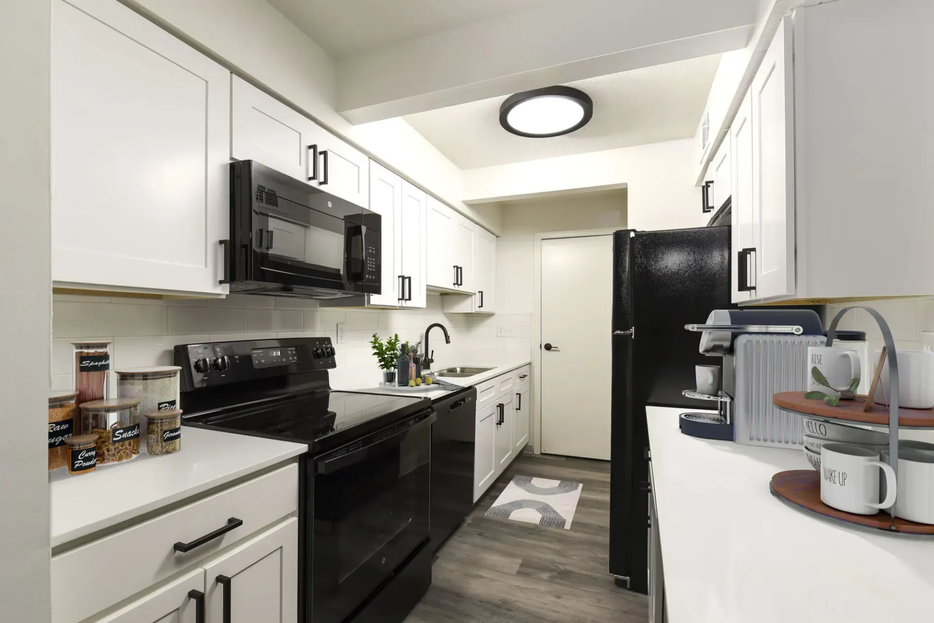 Interior view of a modern apartment kitchen with white cabinets, black appliances, and a sink.