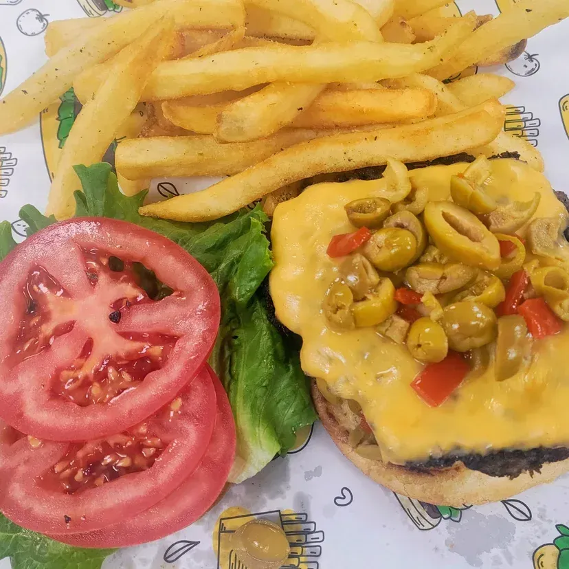 Burger with fries, tomato slices, lettuce, and olives, on a printed paper.