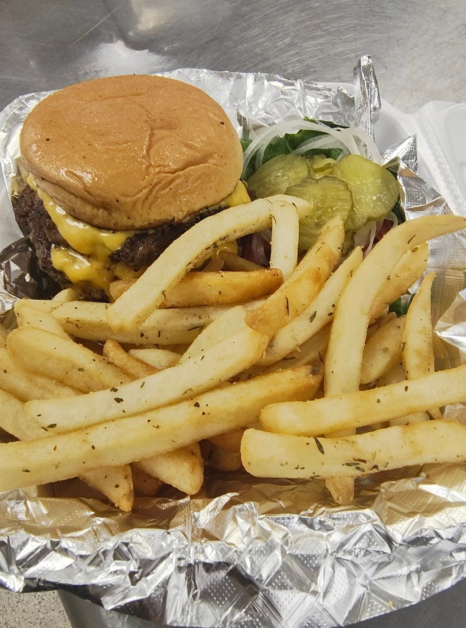 Cheeseburger with fries, pickles, and onions in foil container.