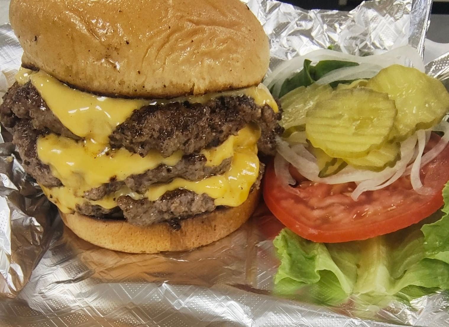 Double cheeseburger with toppings of tomato, pickles, and onion.