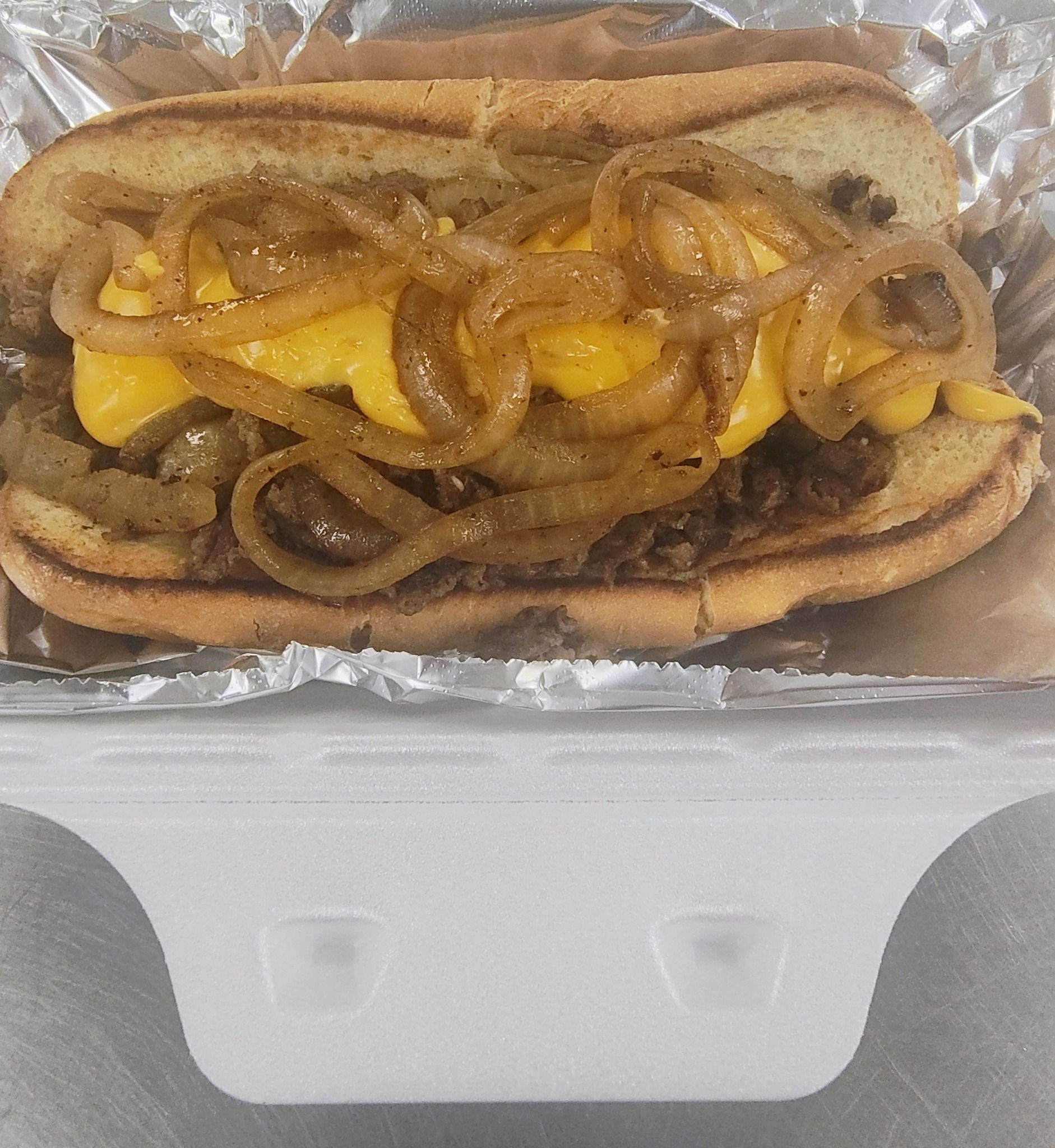 Cheesesteak sandwich with caramelized onions and melted cheese in a styrofoam container.