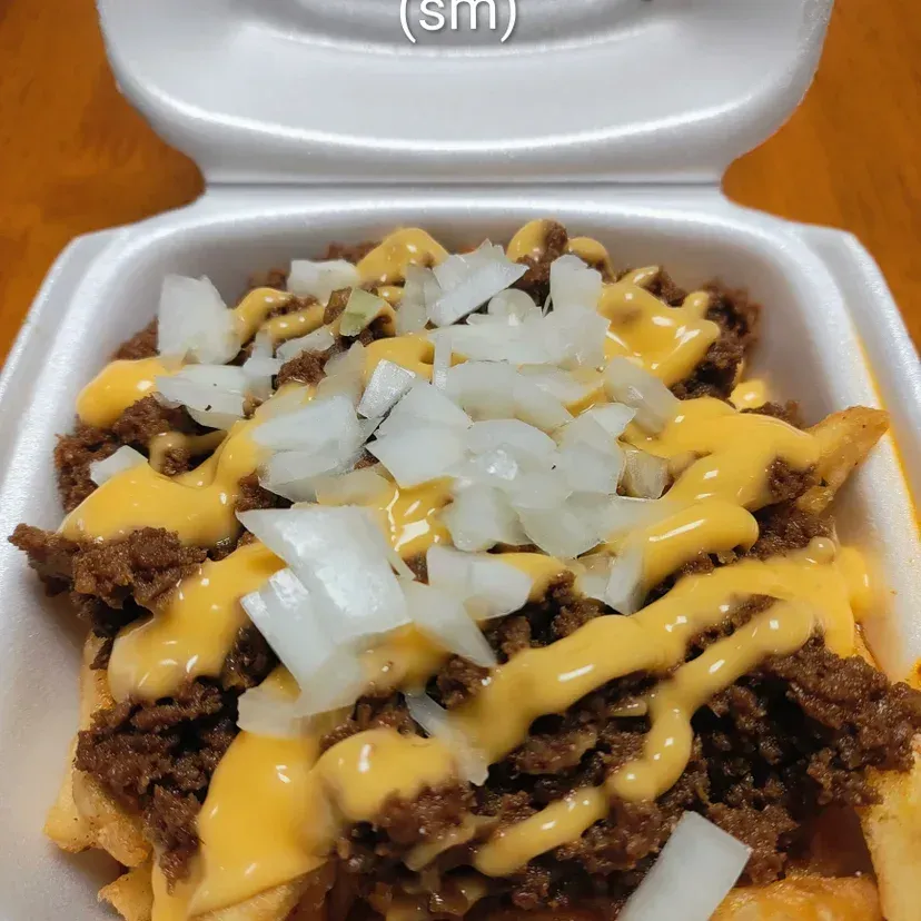 Chili cheese fries with diced onions, served in a styrofoam container.