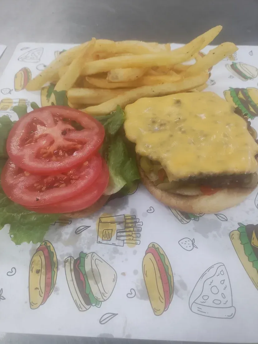 Cheeseburger with tomato slices and fries on patterned paper.