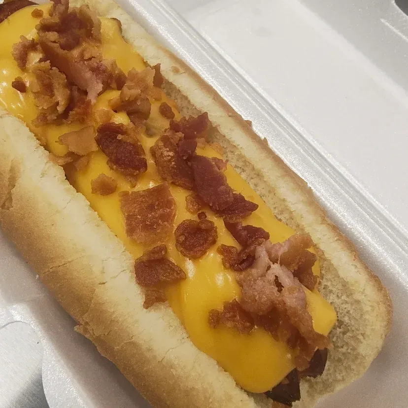 Hot dog in a bun, topped with melted cheese and crumbled bacon.