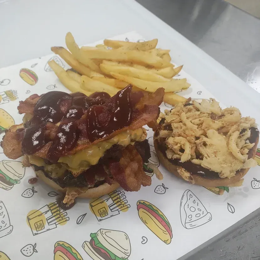 Burger with bacon, cheese, and barbecue sauce; fries; onion rings. Served on a patterned paper.