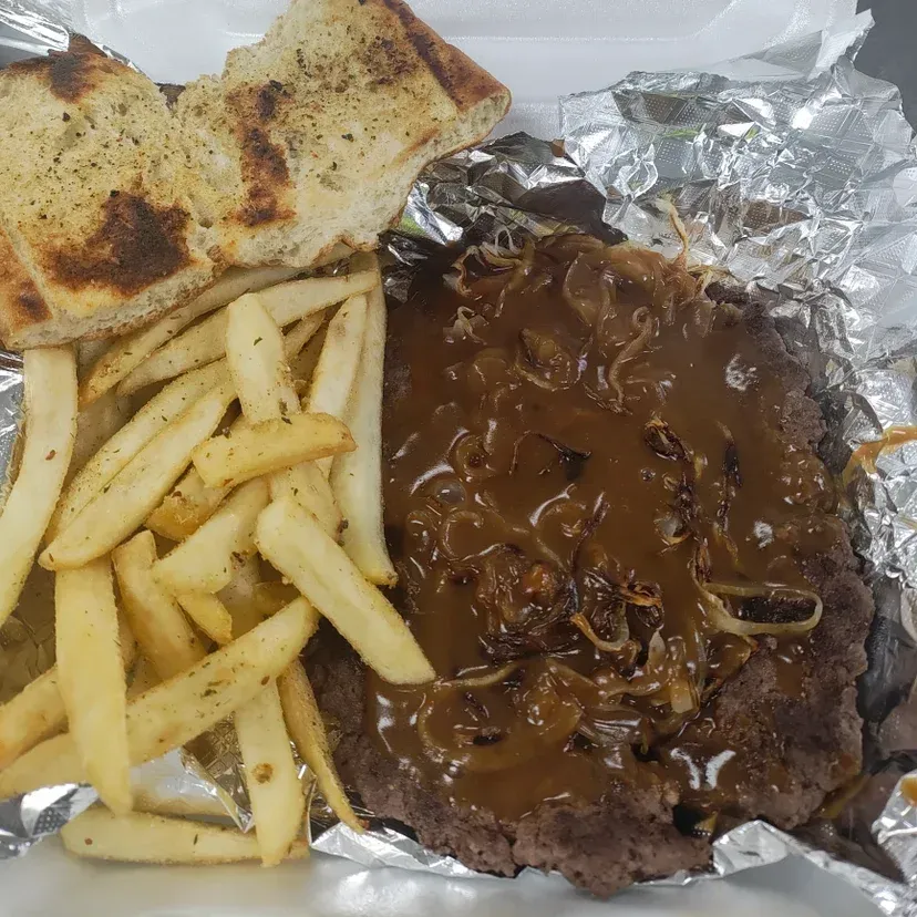 Steak with gravy and onions, fries, and garlic bread in foil container.
