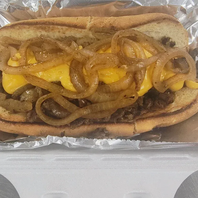 Cheesesteak sandwich with caramelized onions and melted yellow cheese on a toasted hoagie roll.