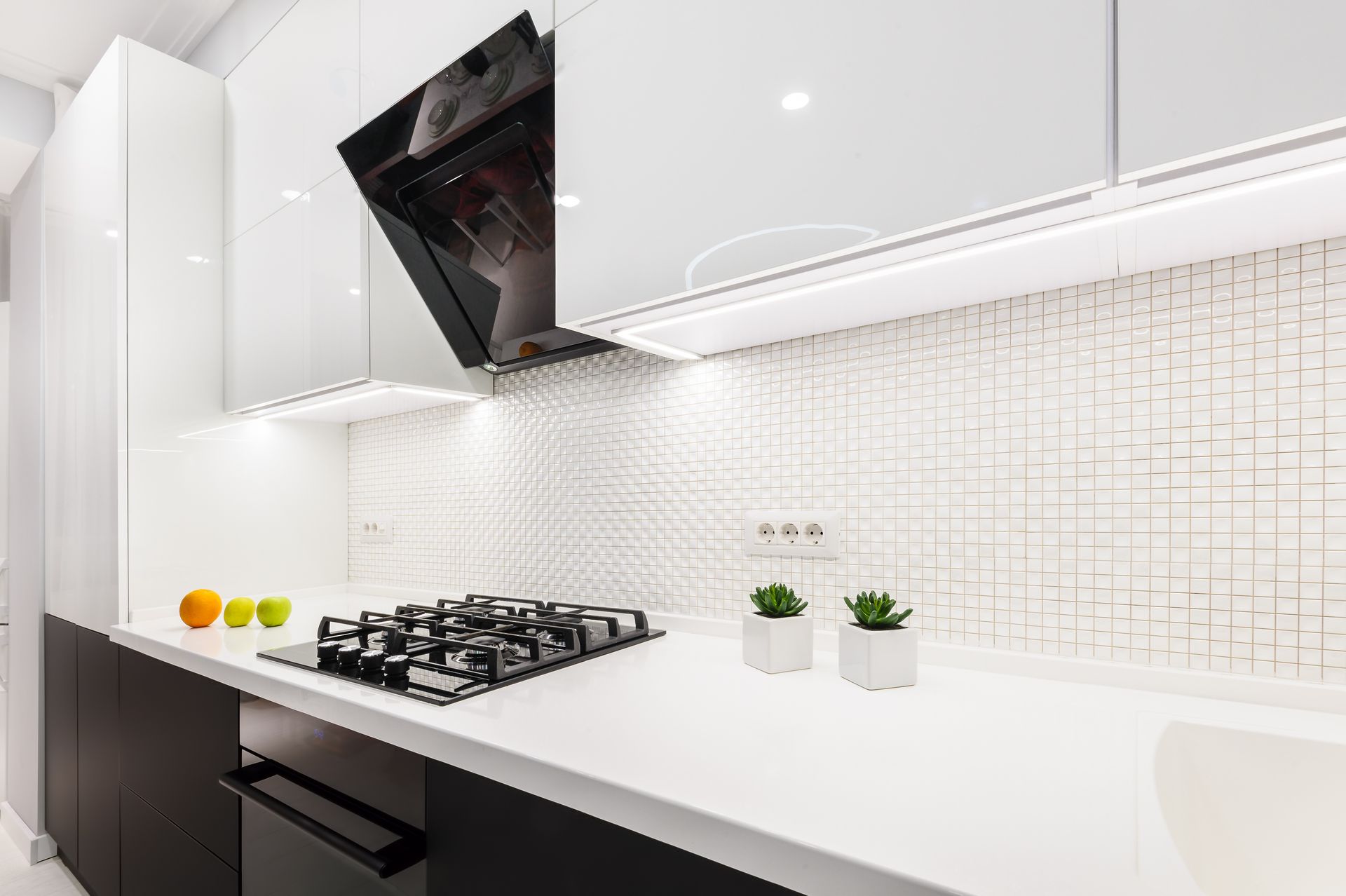 A modern kitchen featuring black lower cabinets, white glossy upper cabinets, a white countertop, and a tiled backsplash.