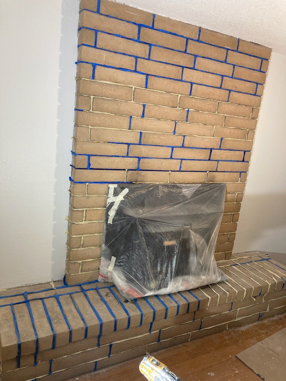 A brick fireplace is being painted with blue tape