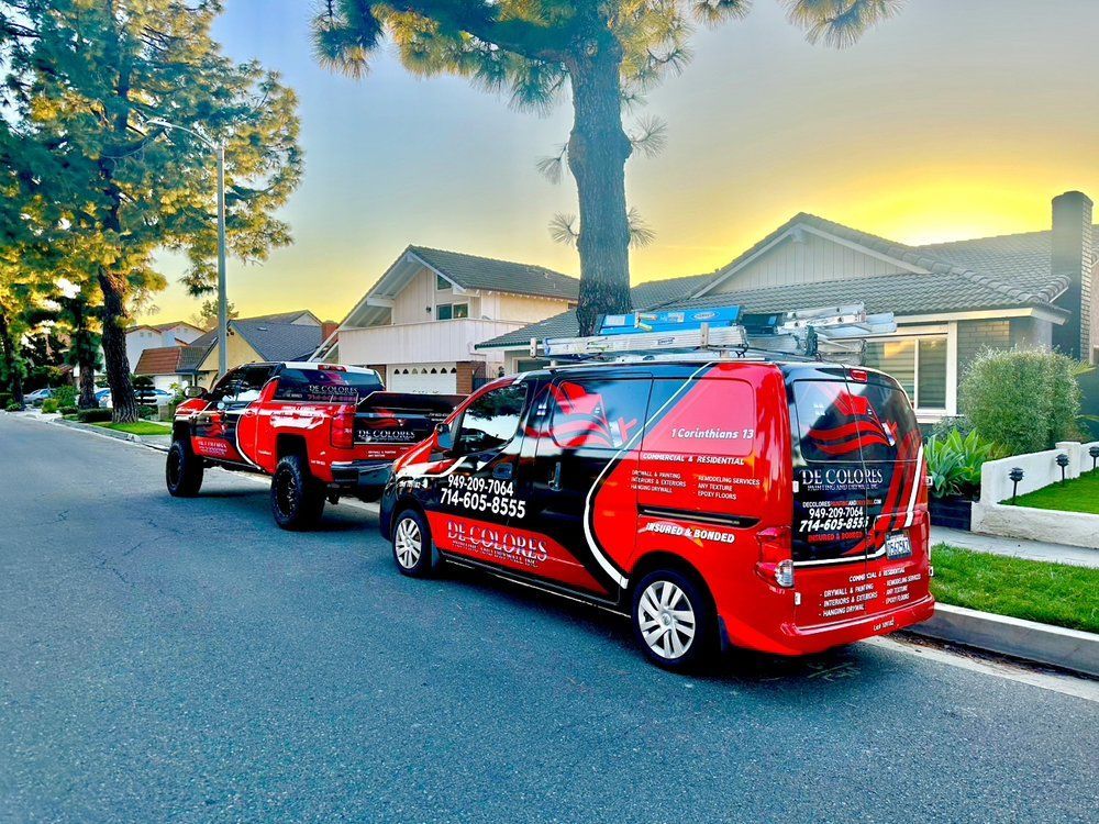 Red service van and truck parked on a street, house in background, sunset colors.