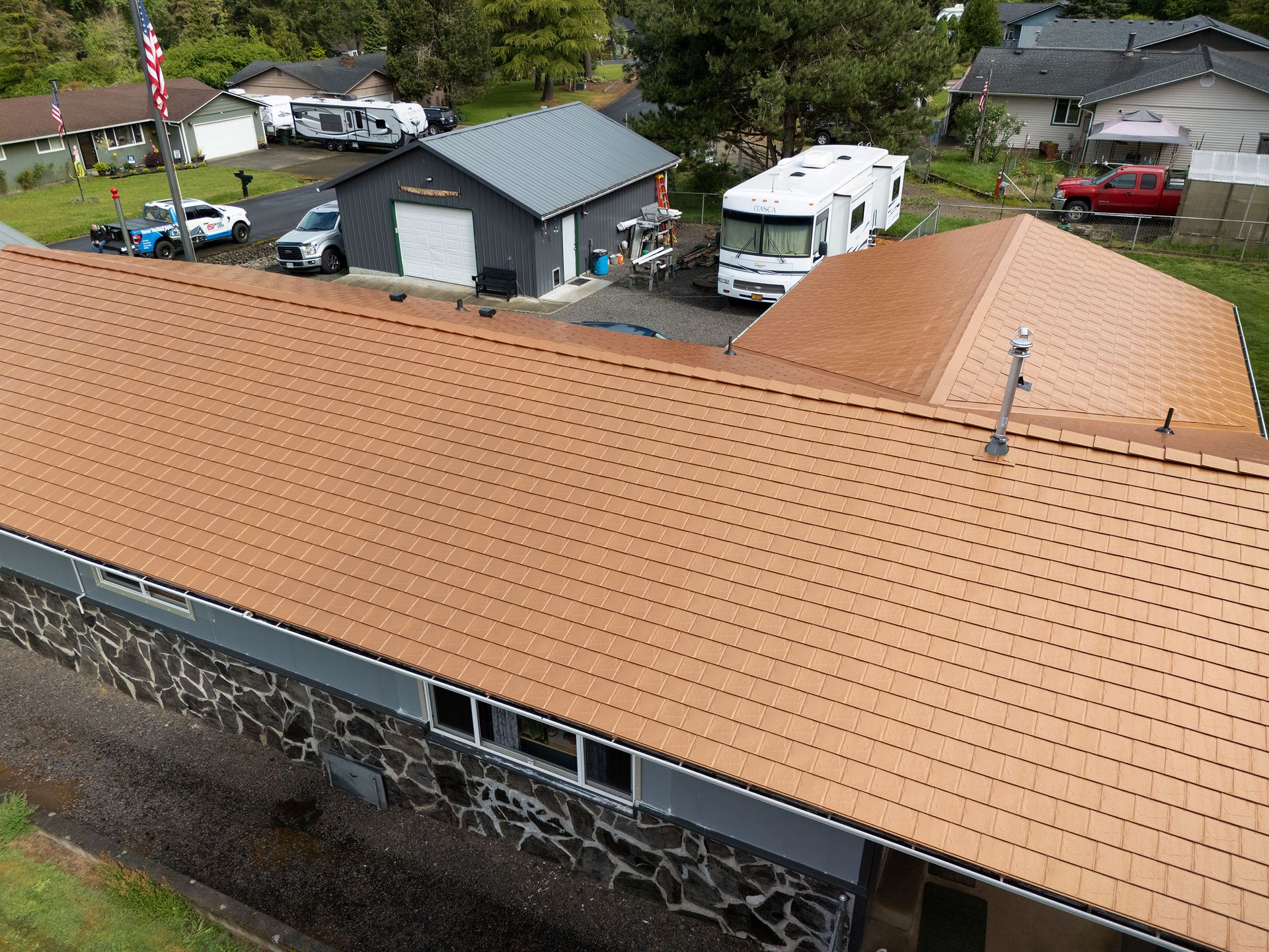 Aerial view of a residential home in the Lexington neighborhood of Castle Rock, WA featuring a Copper Penny Interlock Slate Roof made from heavy-gauge aluminum. The roof installation by Interlock Metal Roofing showcases a rich copper finish with precise interlocking panels and minimal seams, enhancing durability and curb appeal in Cowlitz County.