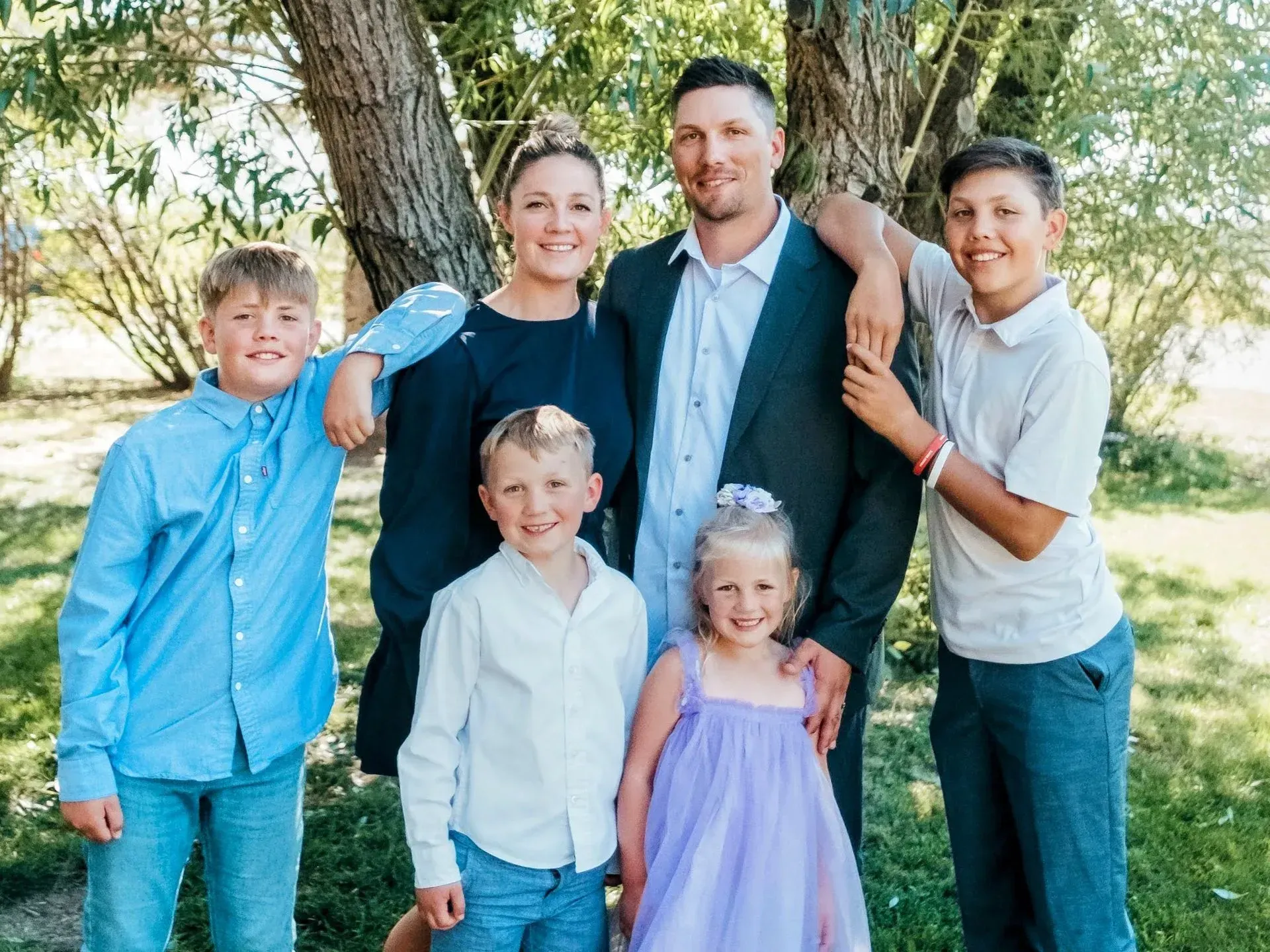 Family of six poses outdoors: parents with four children, smiles.