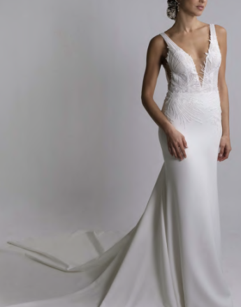 A woman in a white wedding dress is standing in front of a white wall.