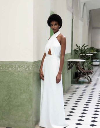 A woman in a white dress is leaning against a wall.