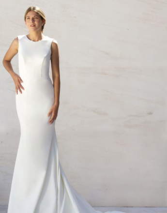 A woman in a white dress is standing in front of a white wall